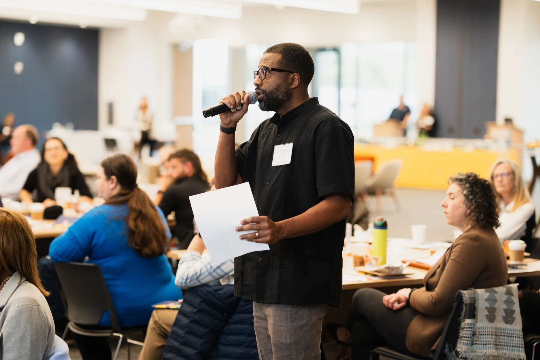 Bavu Blakes speaking among participants seated at tables